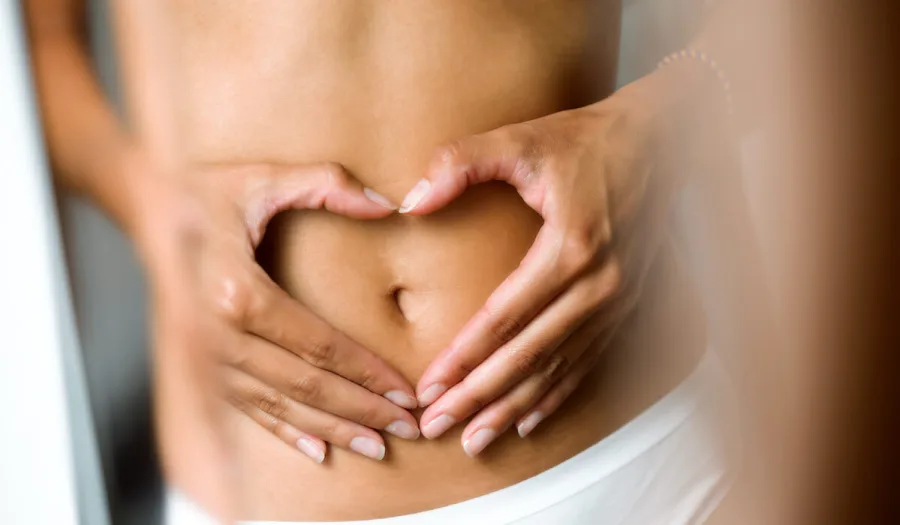 Hände formen ein Herz auf dem Bauch